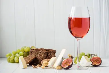 Persona disfrutando de una copa de vino tinto junto a una ensalada fresca y colorida como parte de una dieta cetogénica equilibrada