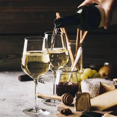 Botella de vino tinto con copa y uvas, destacando los antioxidantes y el resveratrol presentes en el vino que pueden influir en un envejecimiento saludable y la longevidad."