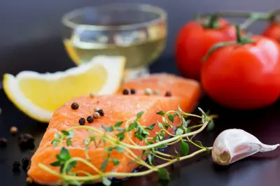 Mujer disfrutando de una copa de vino tinto mientras cena con una ensalada fresca y pescado a la parrilla, ilustrando cómo el vino puede integrarse en una dieta cetogénica equilibrada.