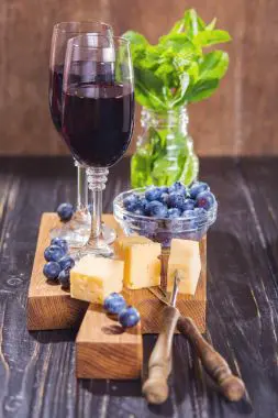 Botella de vino tinto con copa y frutas frescas, resaltando los posibles beneficios antioxidantes y de recuperación muscular del vino después del ejercicio